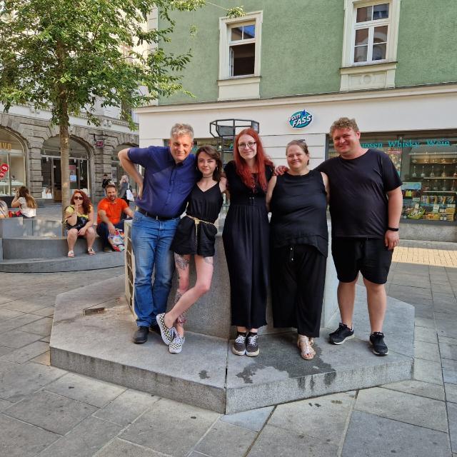 Die 4 Mitglieder des Vorstands und eine Mitarbeiterin von Irren ist menschlich e.V. stehen vor einem Brunnen in der Regensburger Altstadt.